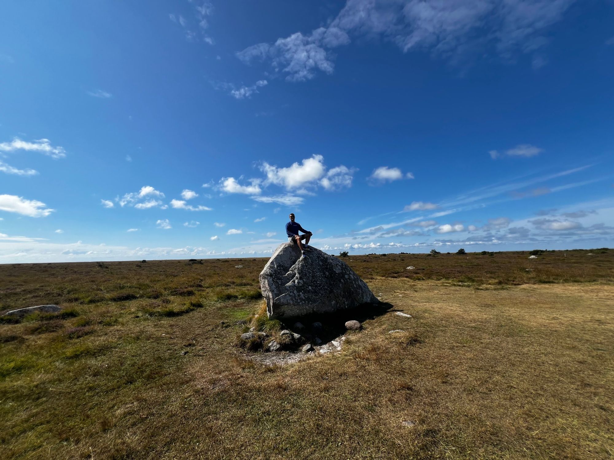 A figure seated on a granite boulder on open heathland under a blue sky