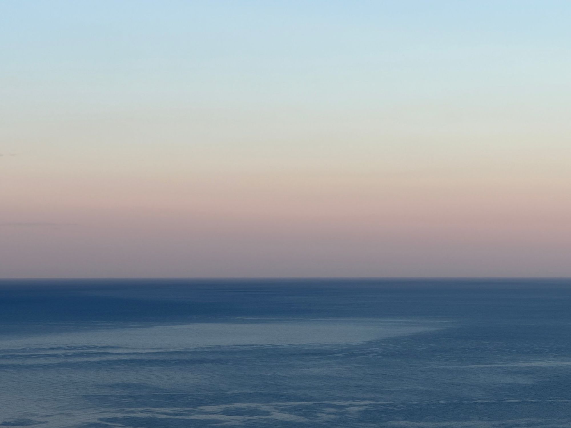 Open sea meeting a pale pink and blue sky at dusk